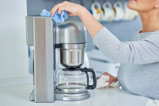 An image of a person cleaning a drip filter coffee machine with a blue cloth