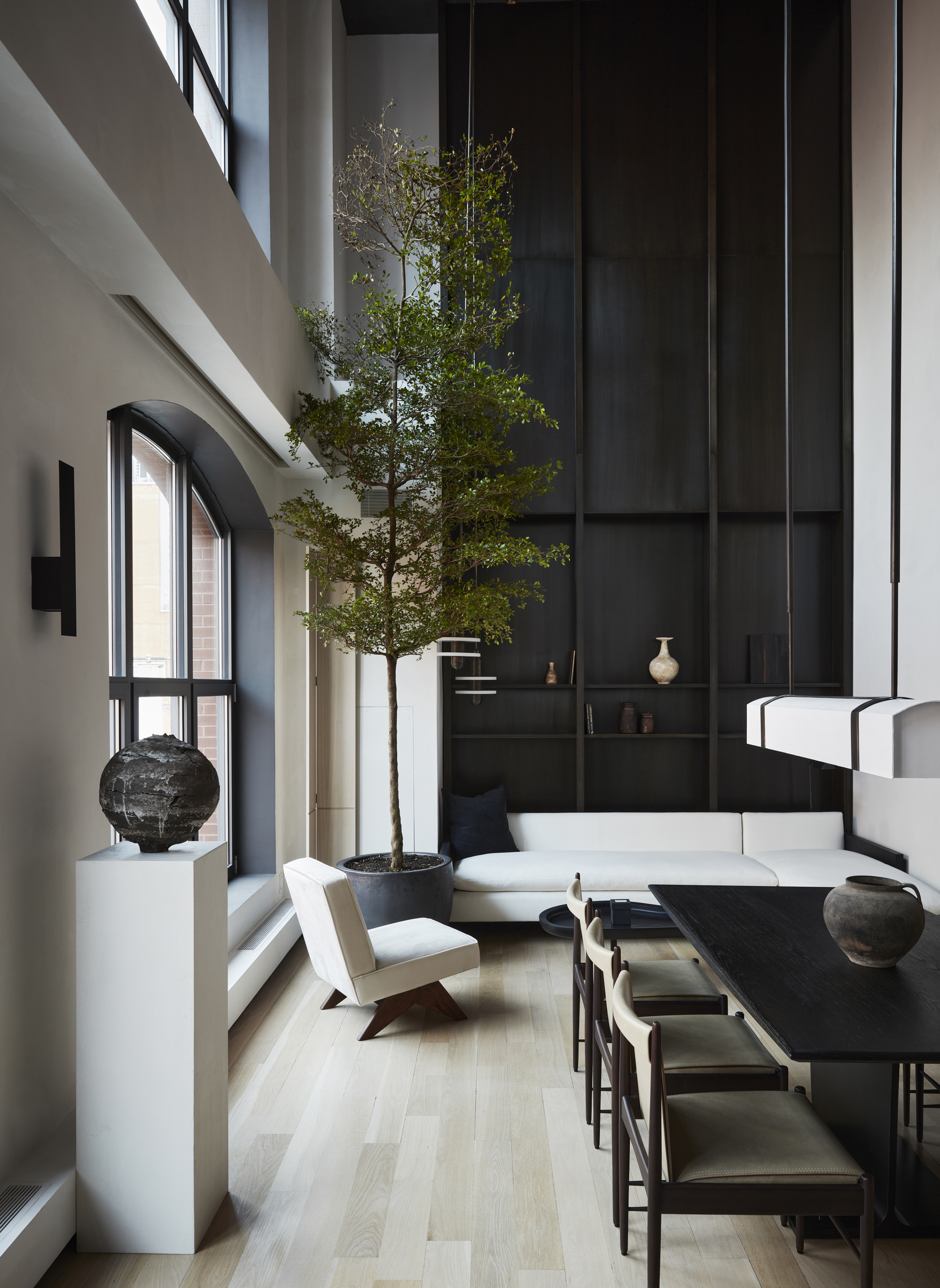 An black and white open planing living / dining area with tall ceilings and a large indoor tree