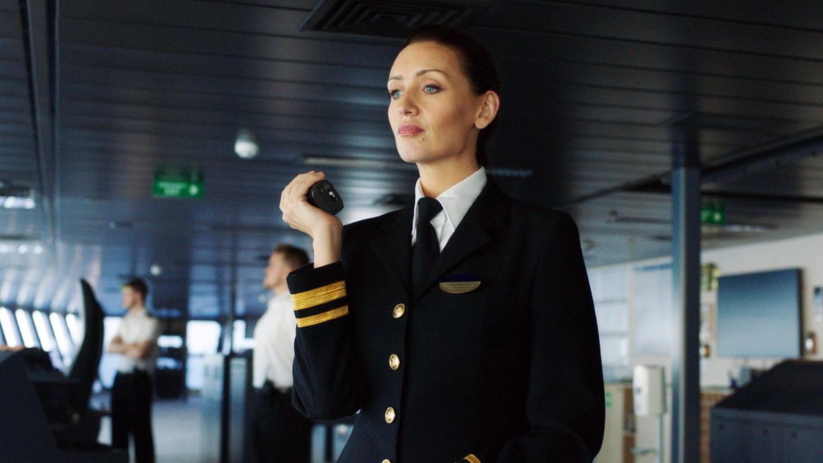 First Officer Kate Woods (Catherine Tyldesley) stands on the bridge of the cruise ship, in full uniform with blazer, holding a radio that she&#039;s speaking into