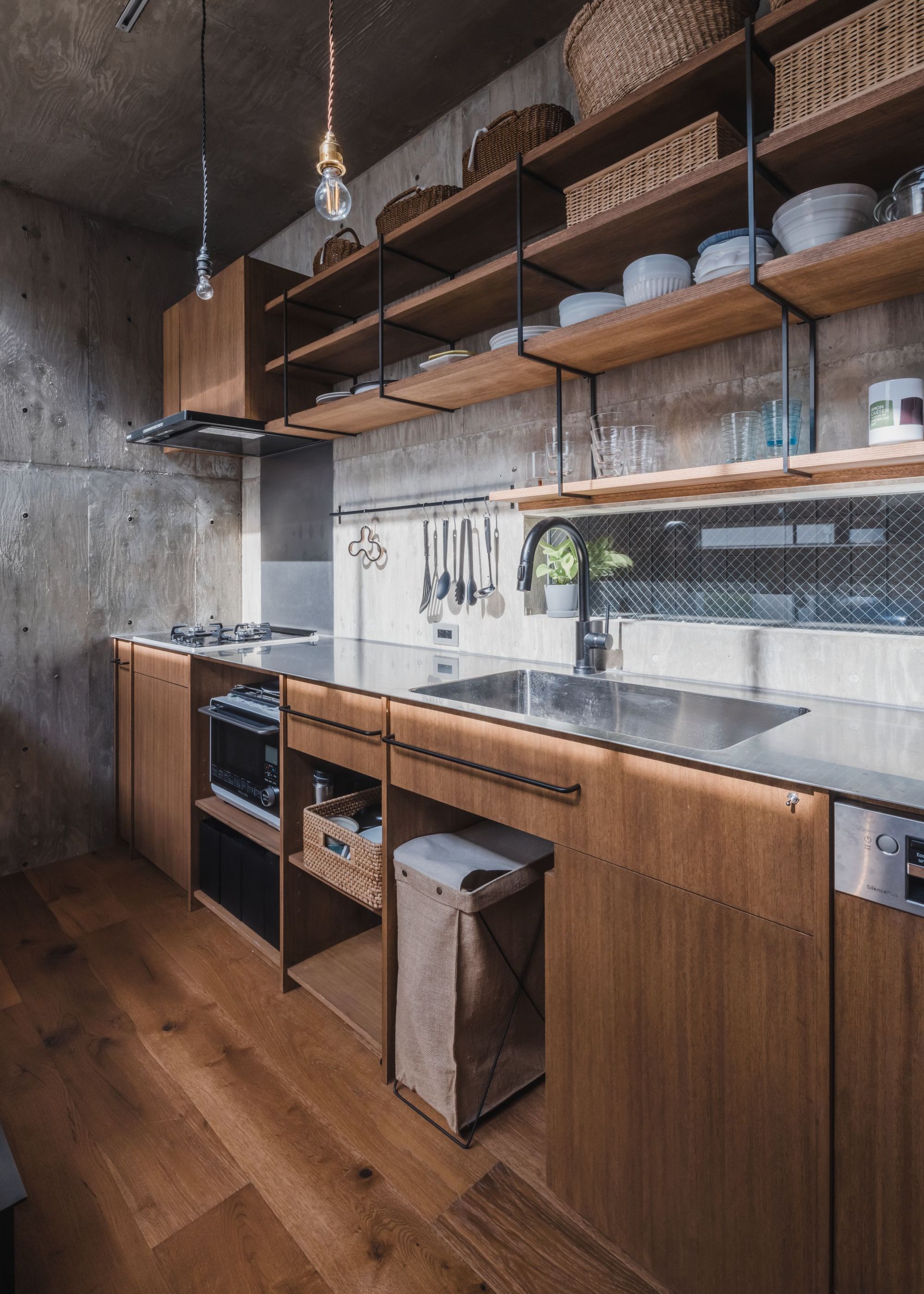 A minimalist Japanese kitchen with concrete walls and ceiling, wood flooring and cabinetry and open shelving with wicker baskets and crockery neatly arranged