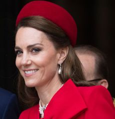 Kate Middleton wearing a red bow coat and hat smiling at the camera on Commonwealth Day 2025