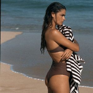 woman wearing a brown bikini and holding a towel on the beach