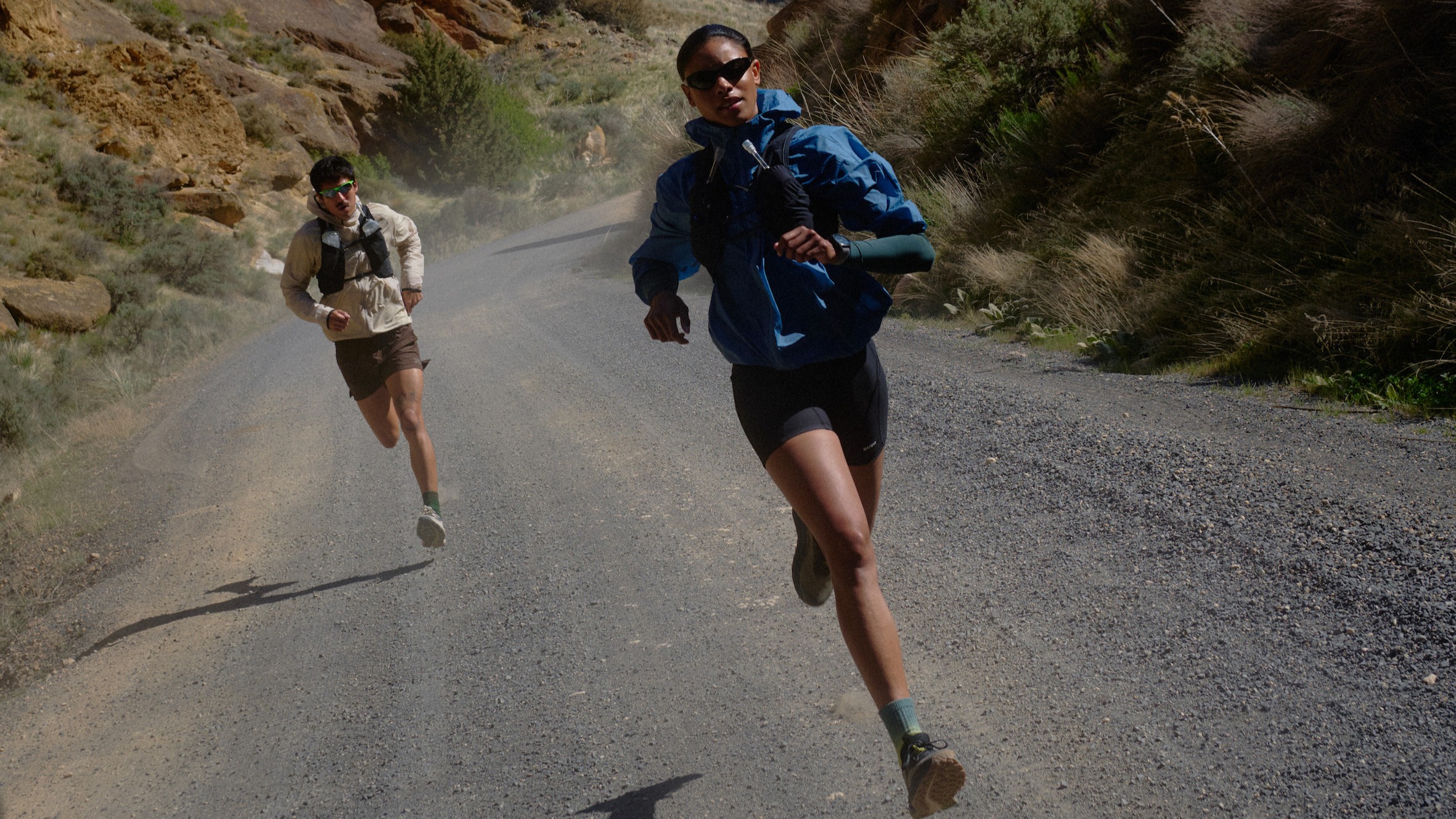 A woman and man running on a gravel road wearing the Keen Seek trail running shoe