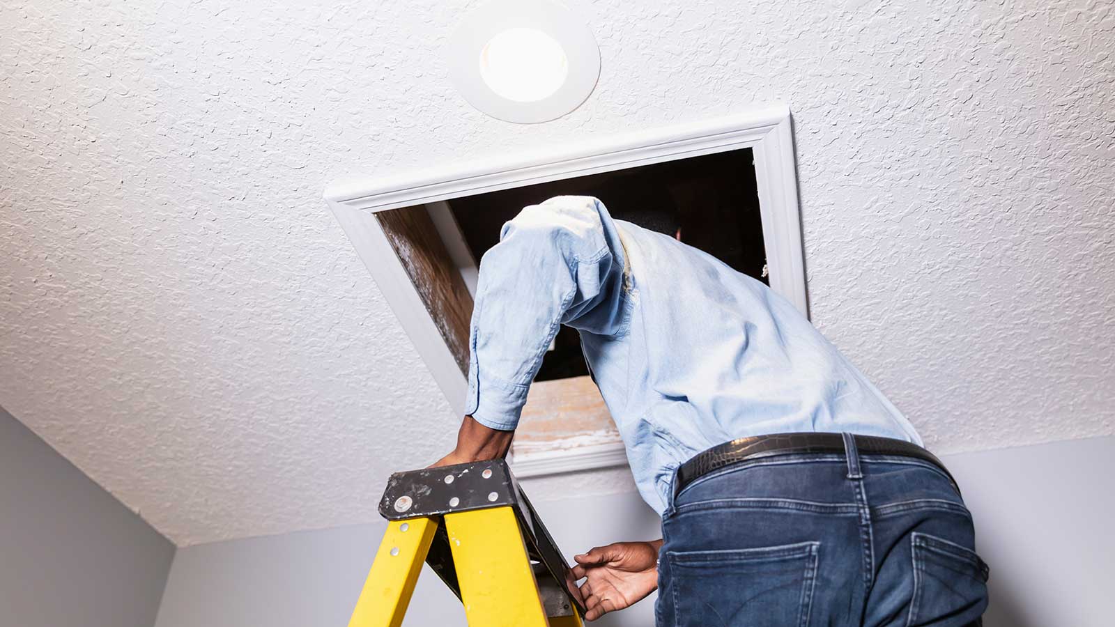 person climbing a ladder to access a small loft hatch