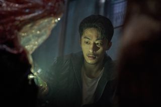 a man (Koo Kyo-hwan as Seol Kang-woo) shines a phone flashlight on a corpse in a clear bag, in 'parasyte the grey'