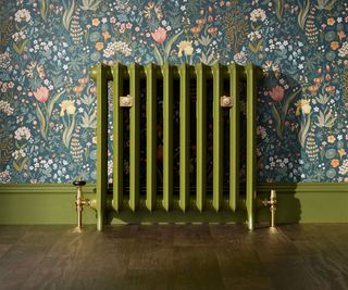 green school radiator in room with matching green skirting, multicolour floral wallpaper and wooden floor