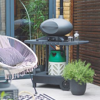 outdoor space with BBQ on wheels, garden armchair, blue and white stripe cushions, planters, tiled stone floor