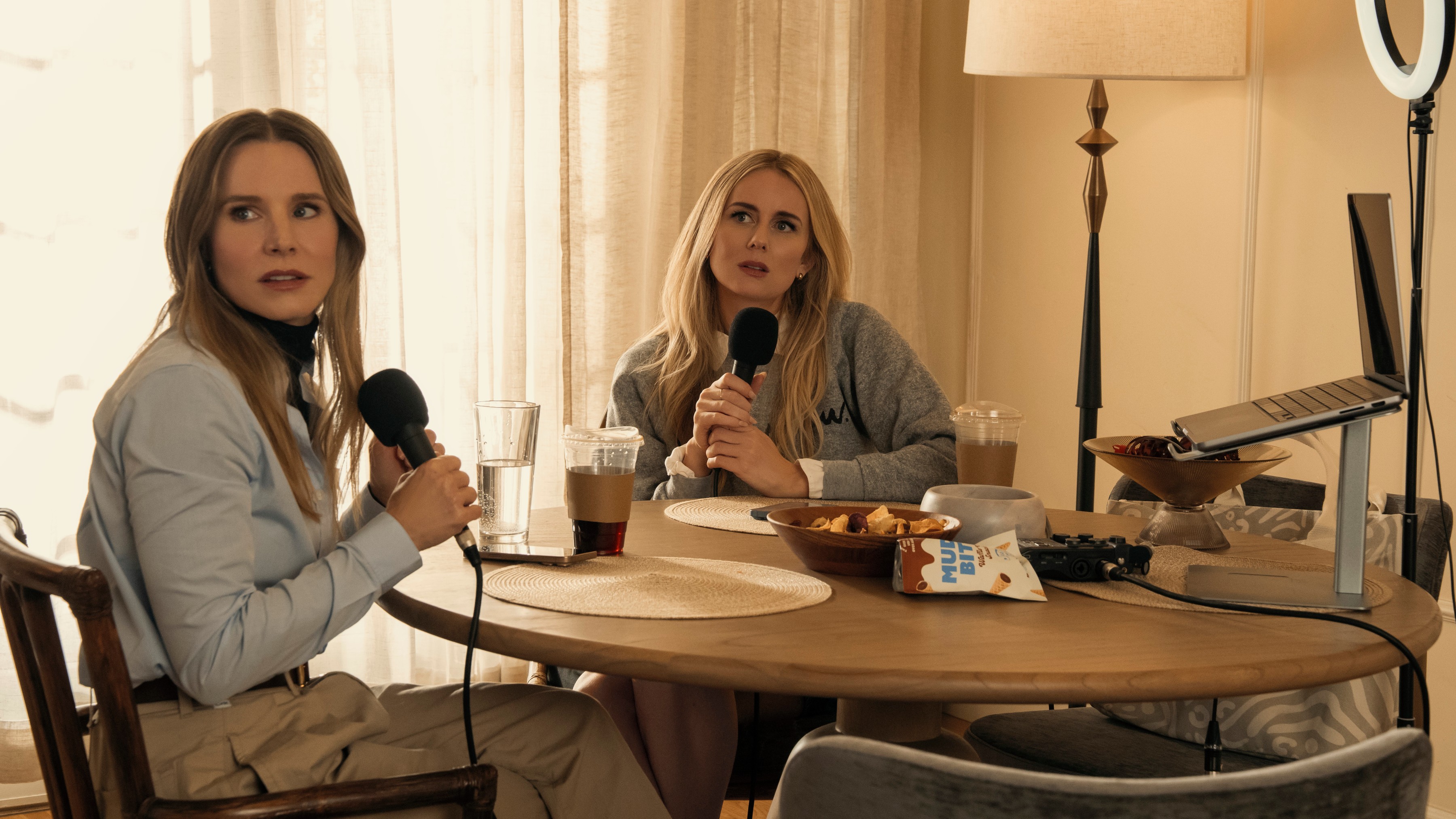 L-R: Joanne (Kristen Bell) and Morgan (Justine Lupe) sit at a table recording a podcast in a scene from "Nobody Wants This" season 2