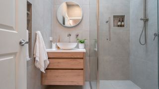 a clean modern bathroom with gray walls, a wooden vanity, round mirror and an open shower