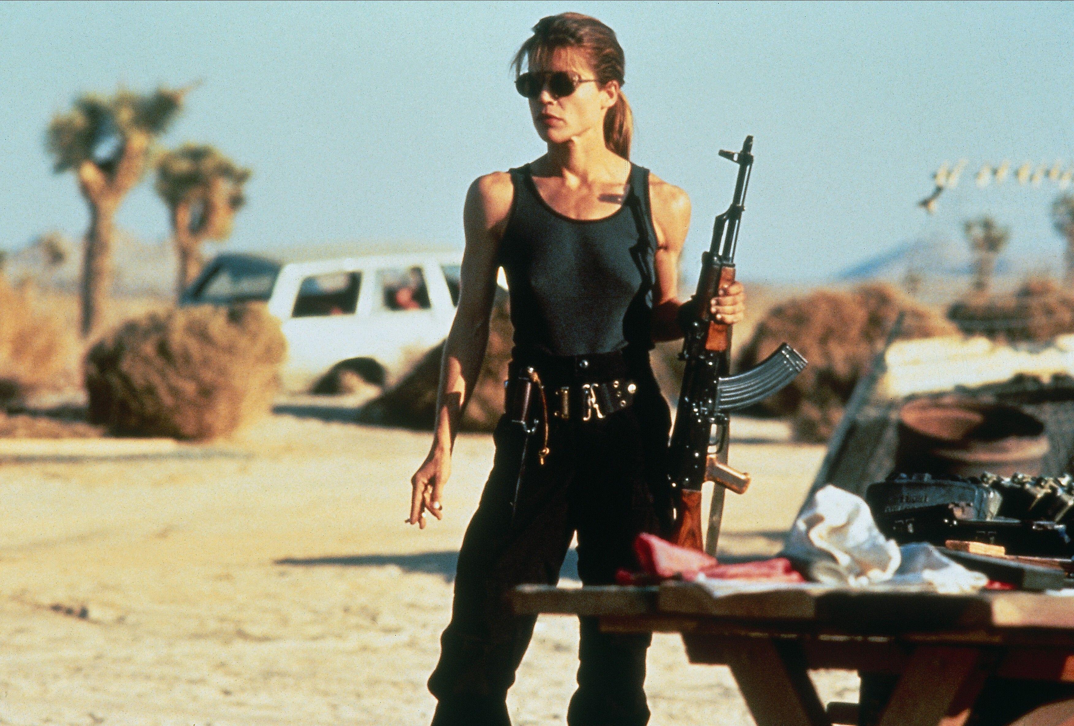 LINDA HAMILTON holding a gun in a parking lot wearing a tank top and black pants as sarah connor in an iconic photo from TERMINATOR 2: JUDGMENT DAY
