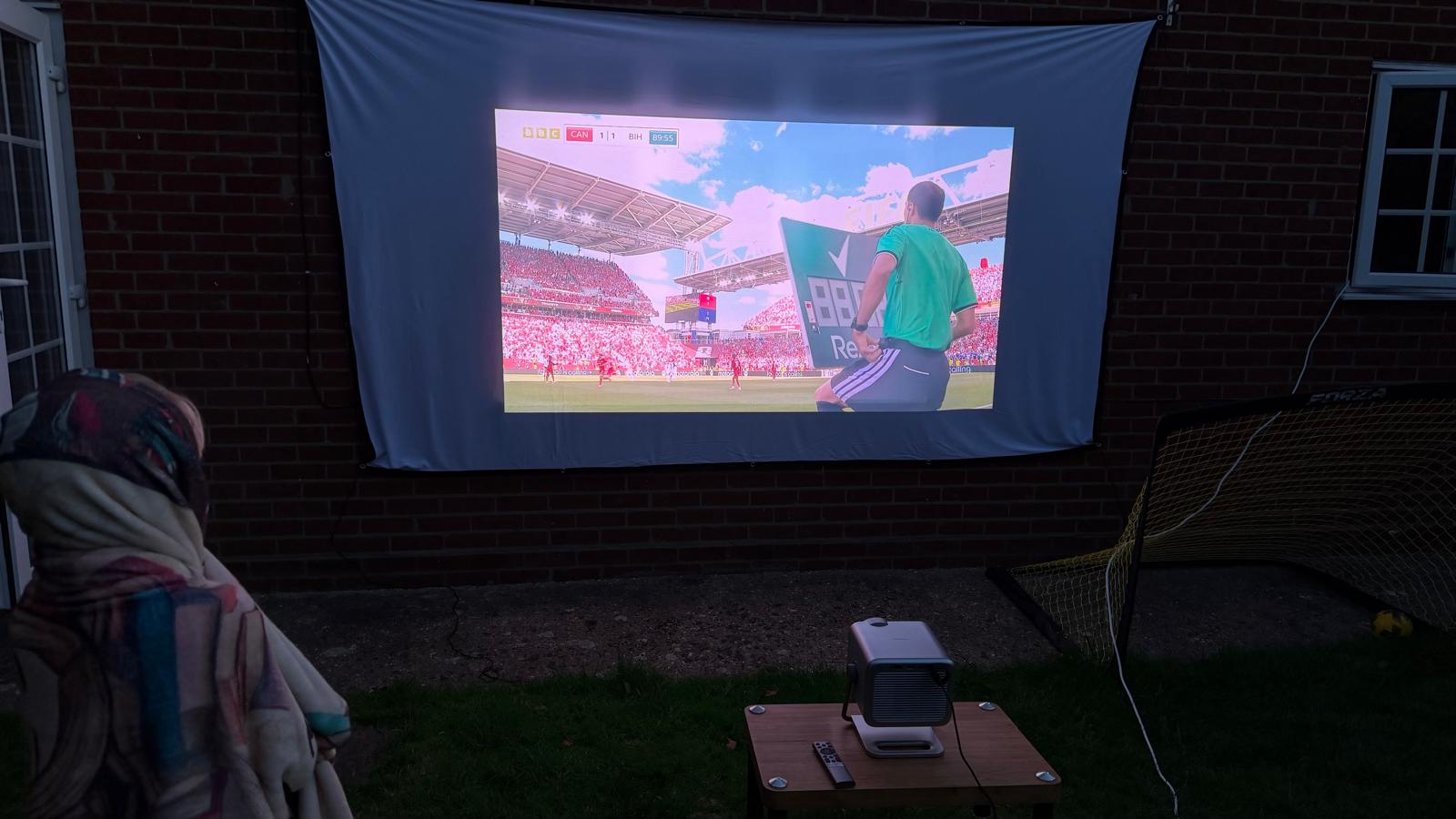 A photo of football being projected onto a white sheet against the wall of a house in a garden