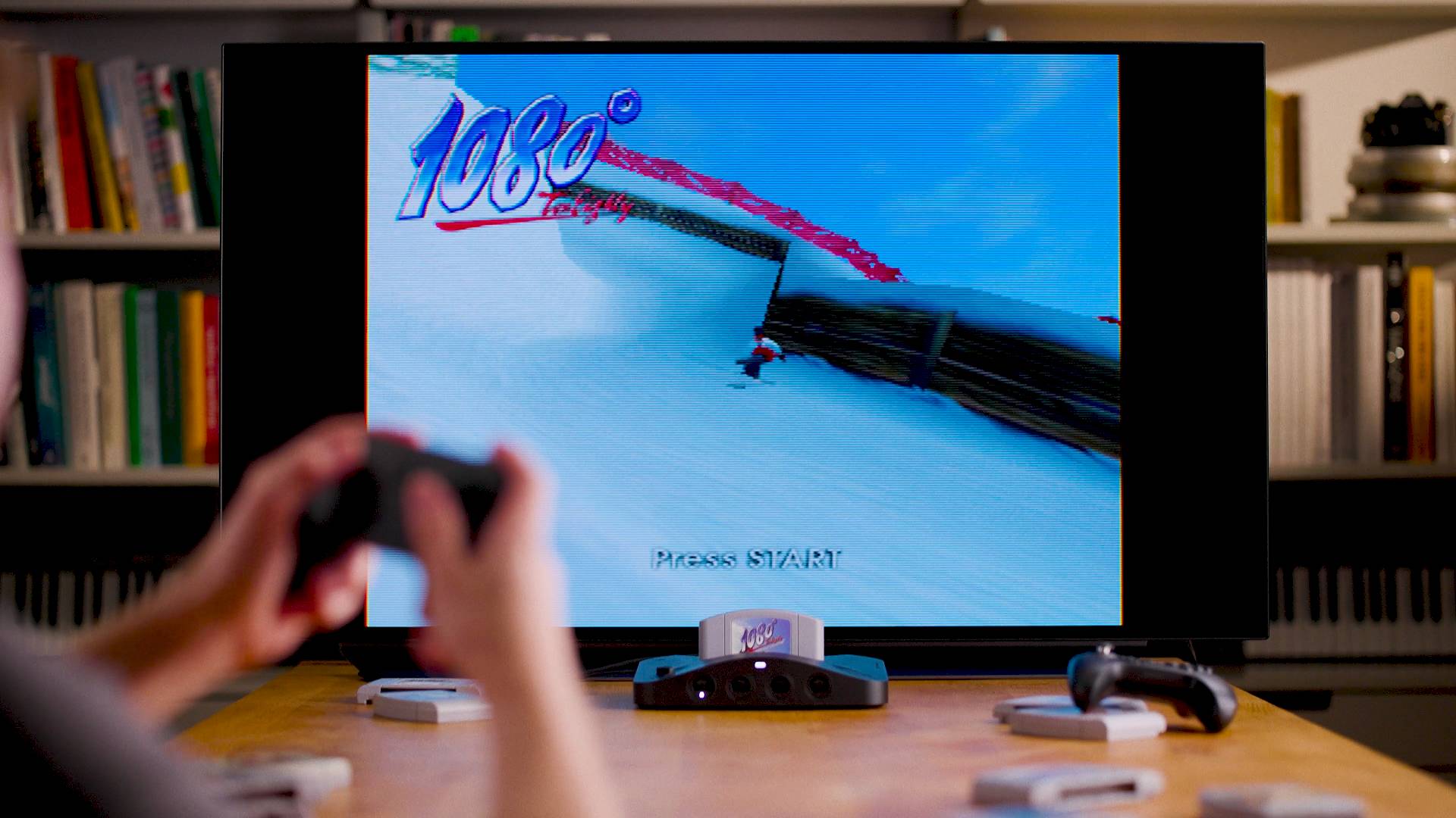 Analogue 3D connected to TV next to 8Bitdo controller and cartridges with player using gamepad in front of screen.