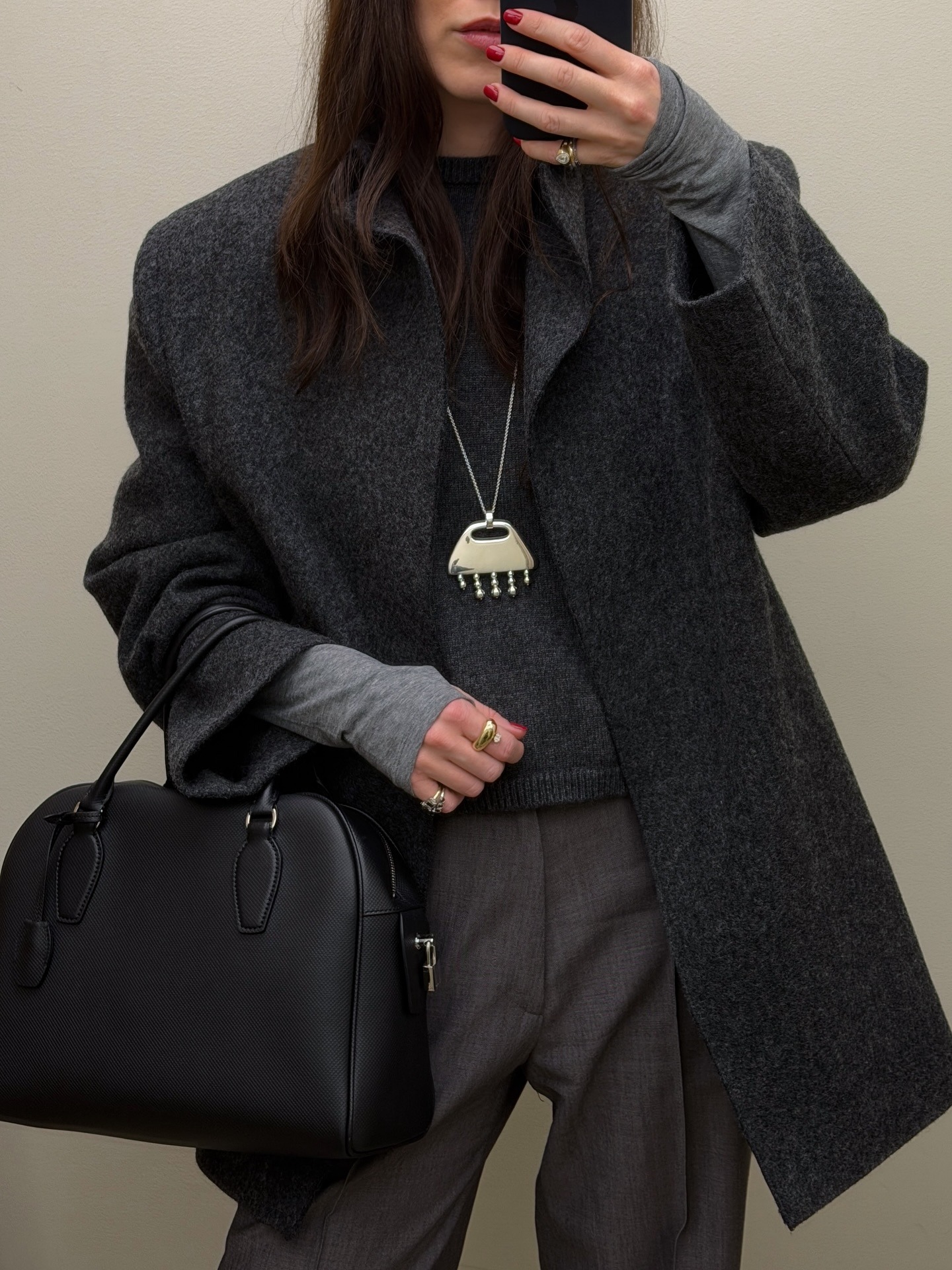 Woman in a gray coat and pants with a silver long pendant necklace.