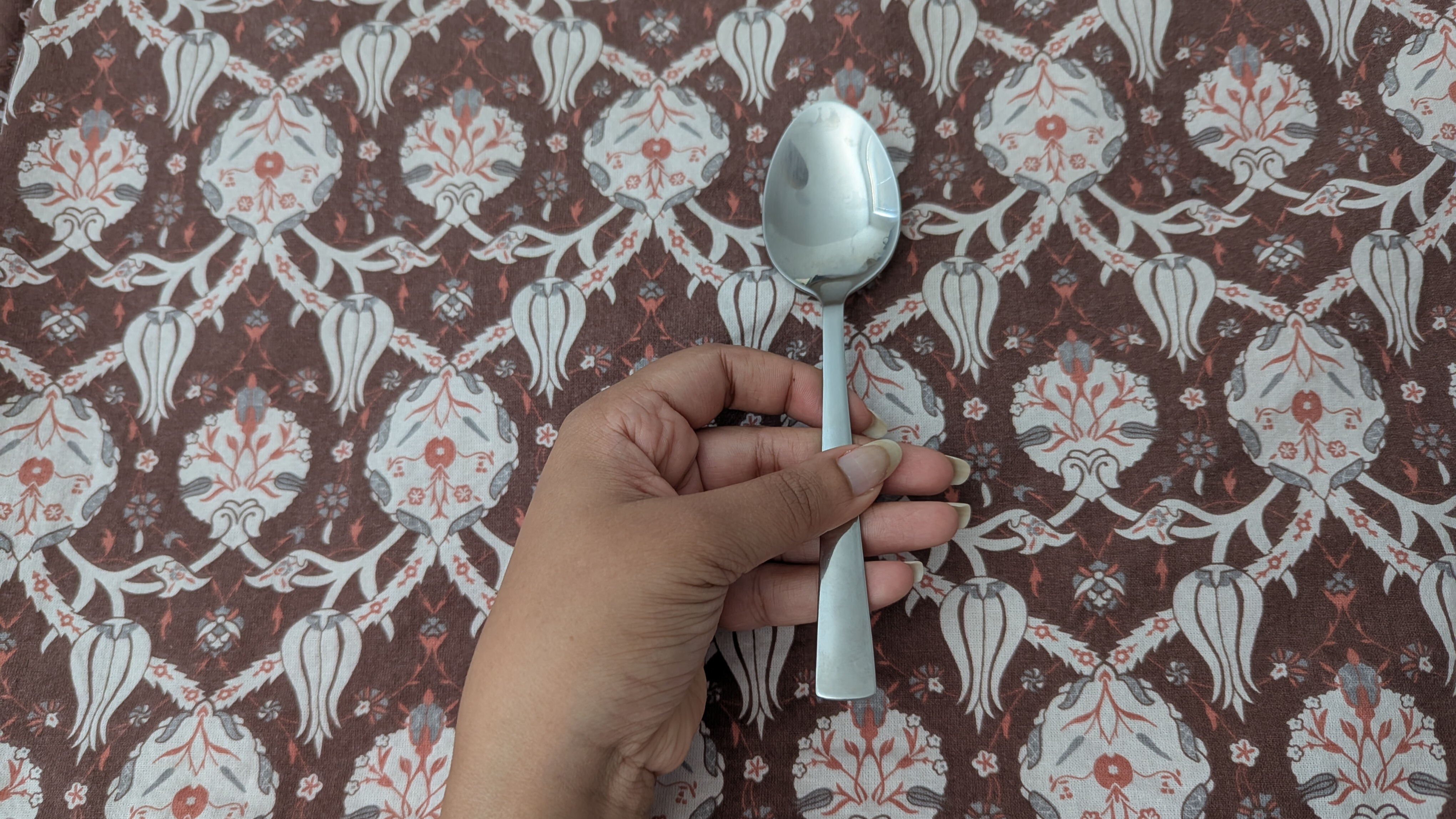 Hand holding a metal spoon against a print brown backdrop