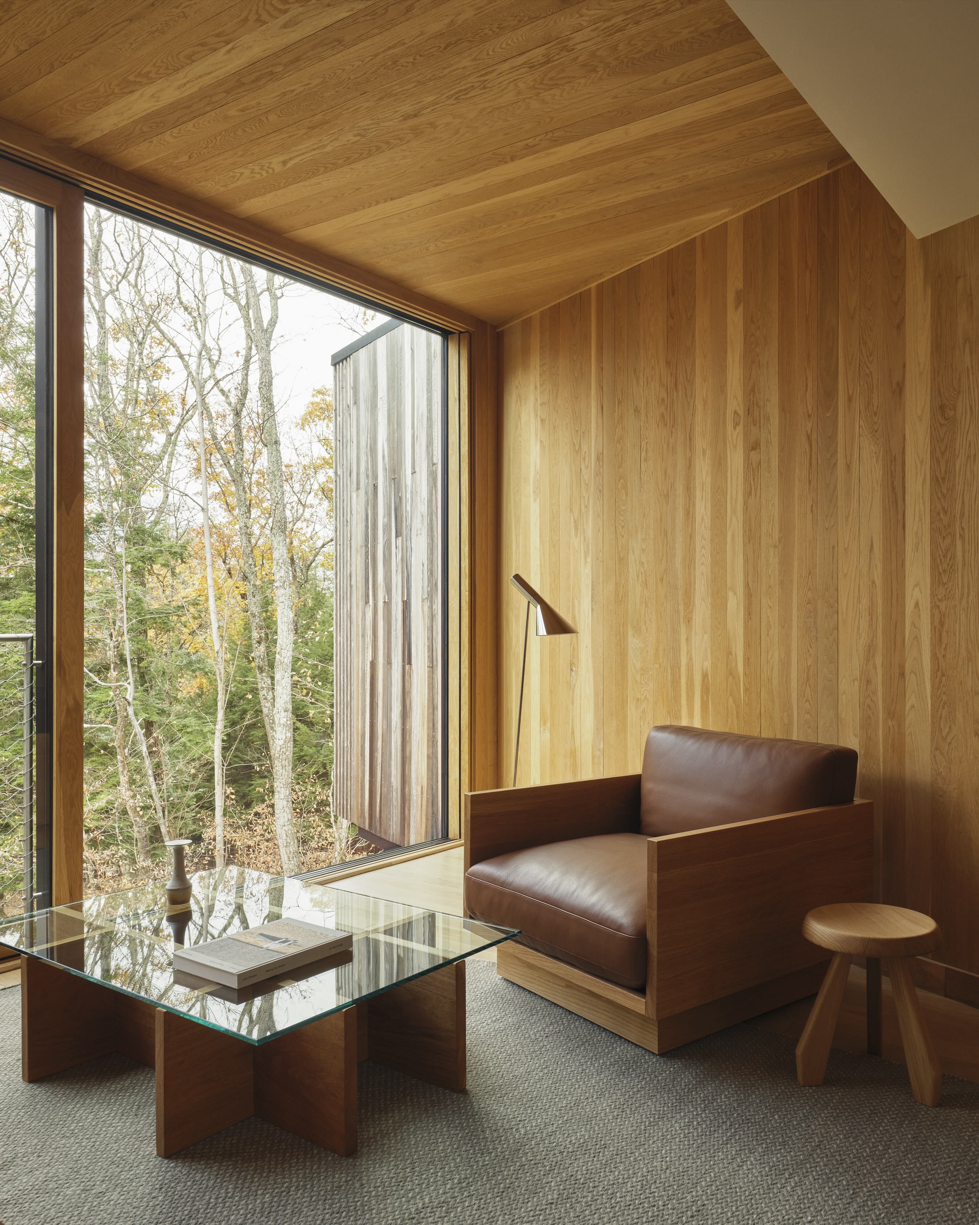 A glass wooden table and an armchair in front of a window overlooking a forest.