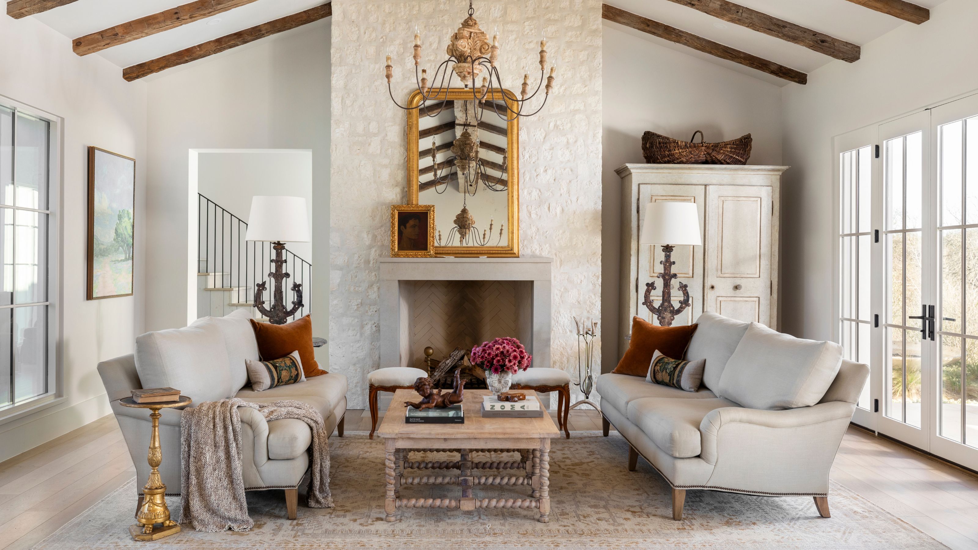 a farmhouse ranch living room with a large stone fireplace, two neutral sofas facing a wooden coffee table and a vintage style cabinet
