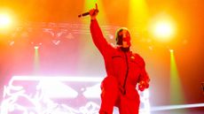 One member of Irish hip hop trio Kneecap, onstage during the 2025 Coachella music festival, wears a Palestinian flag baclava and raises hand with microphone