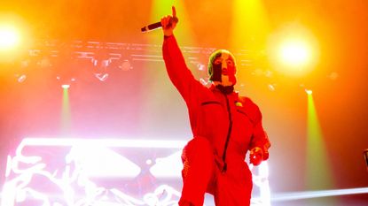One member of Irish hip hop trio Kneecap, onstage during the 2025 Coachella music festival, wears a Palestinian flag baclava and raises hand with microphone