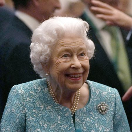 Queen Elizabeth laughs while wearing a turquoise floral embroidered jacket while Boris Johnson looks pensive in a black suit