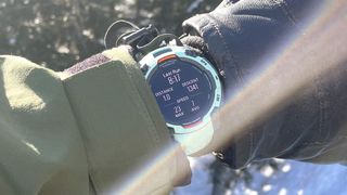 Garmin Instinct 3 on a user's wrist shown up-close in between a ski glove and jacket