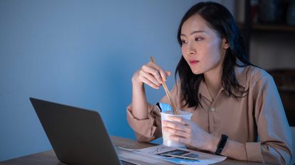 Photo of woman looking at computer and shopping while eating noodles.