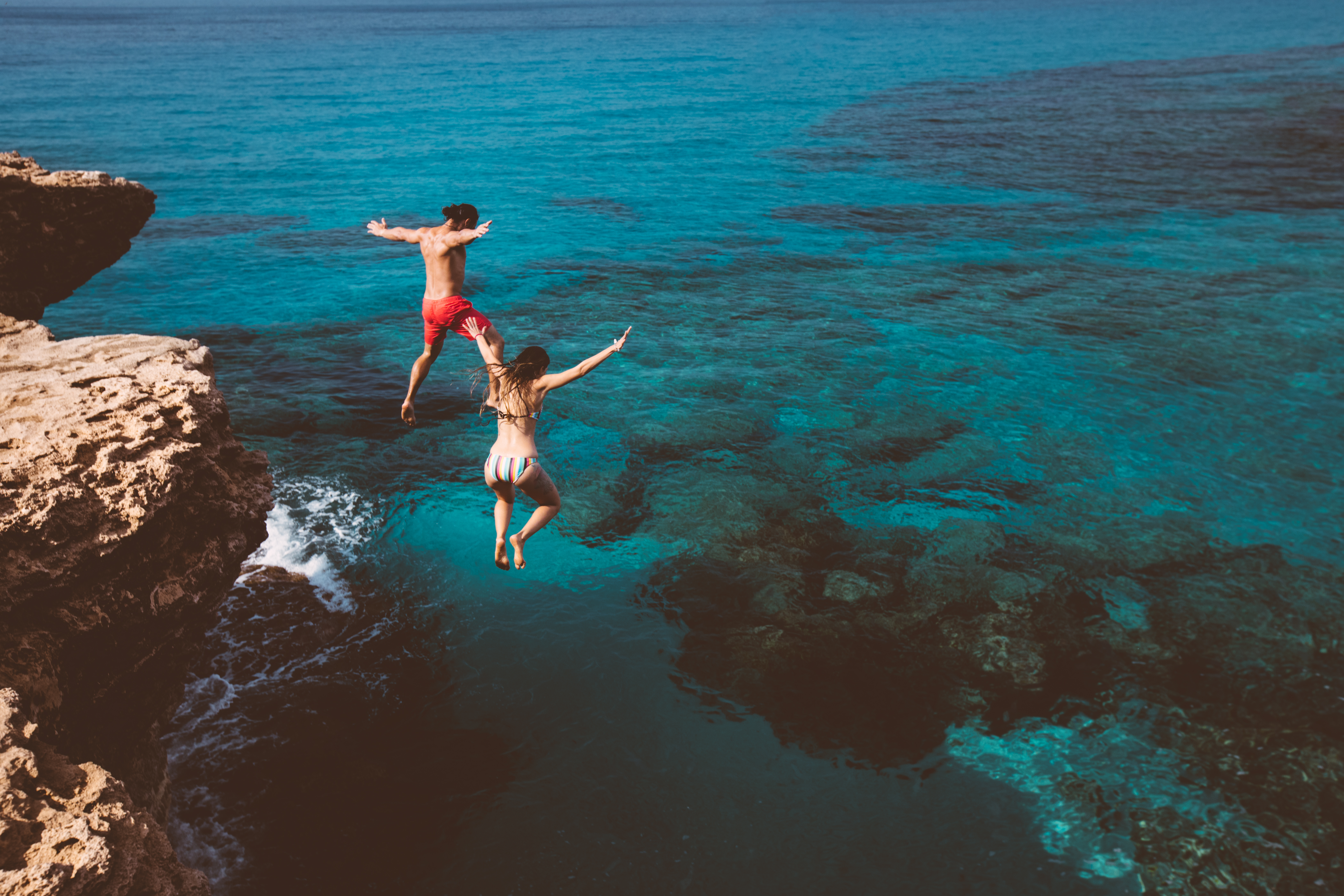 Young couple jumping into the ocean from a rock