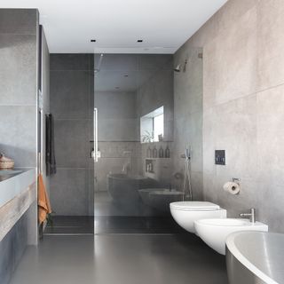 A modern bathroom with grey tiled walls and white sanitaryware, including wall-hung bidet and toilet