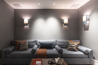 Basement cinema room with sofa neutral sofa and throw pillows, coffee table and wall lights
