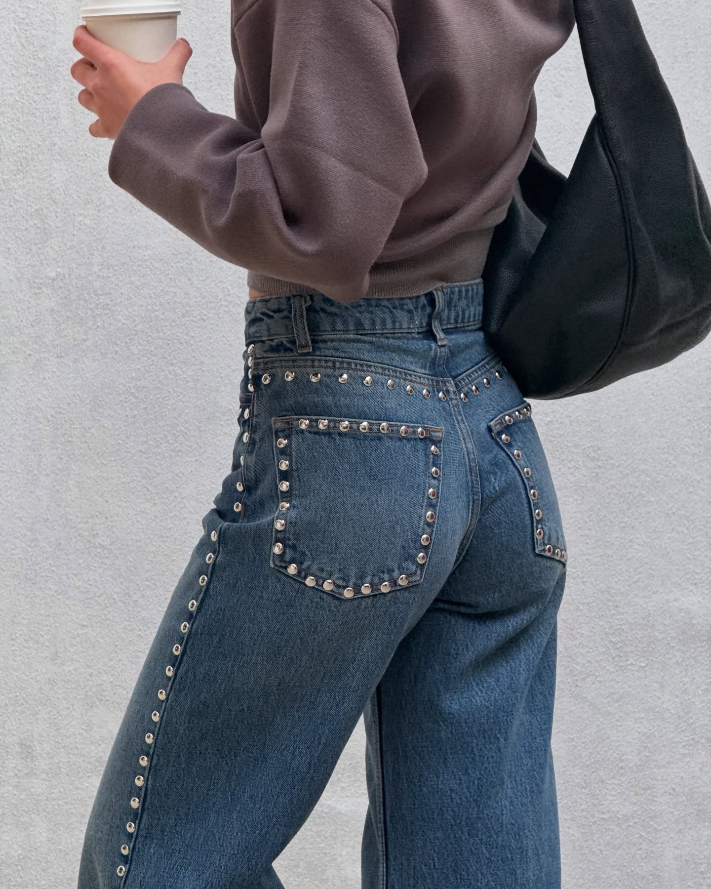 French fashion person Tamara Mory wears blue denim studded jeans, a black leather bag and browny-gray jumper in a recent image from her Instagram.