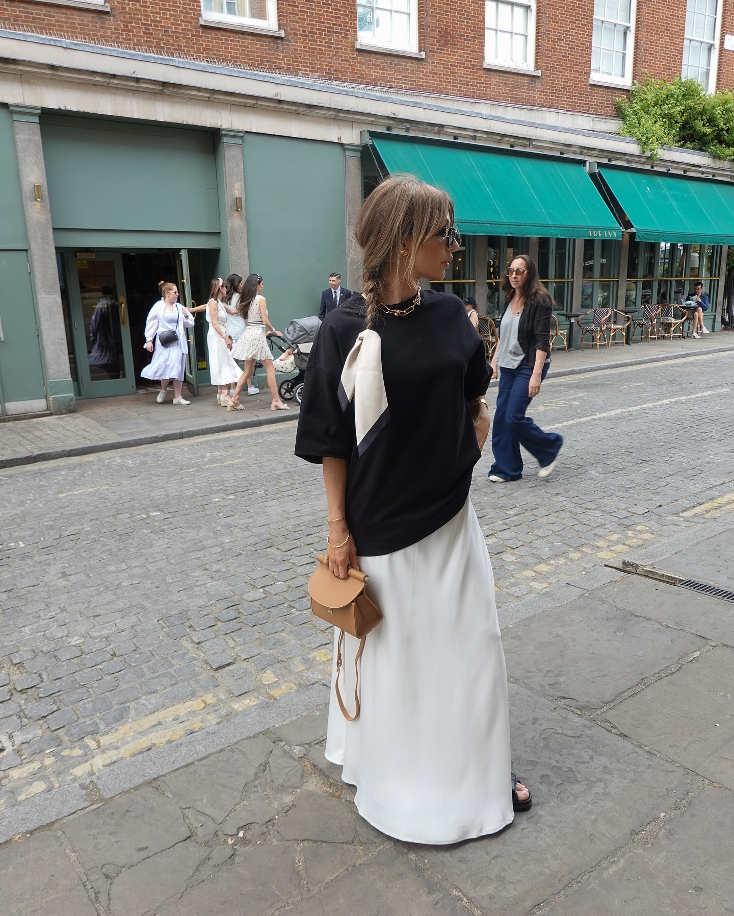 Agnes wearing an oversized black t-shirt, white satin maxi skirt and plaited hair tied with a scarf