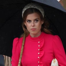 Princess Beatrice wears a red dress and carries a black umbrella while walking in front of sister Princess Eugenie at the Sovereign's Garden Party at Buckingham Palace on May 21, 2024