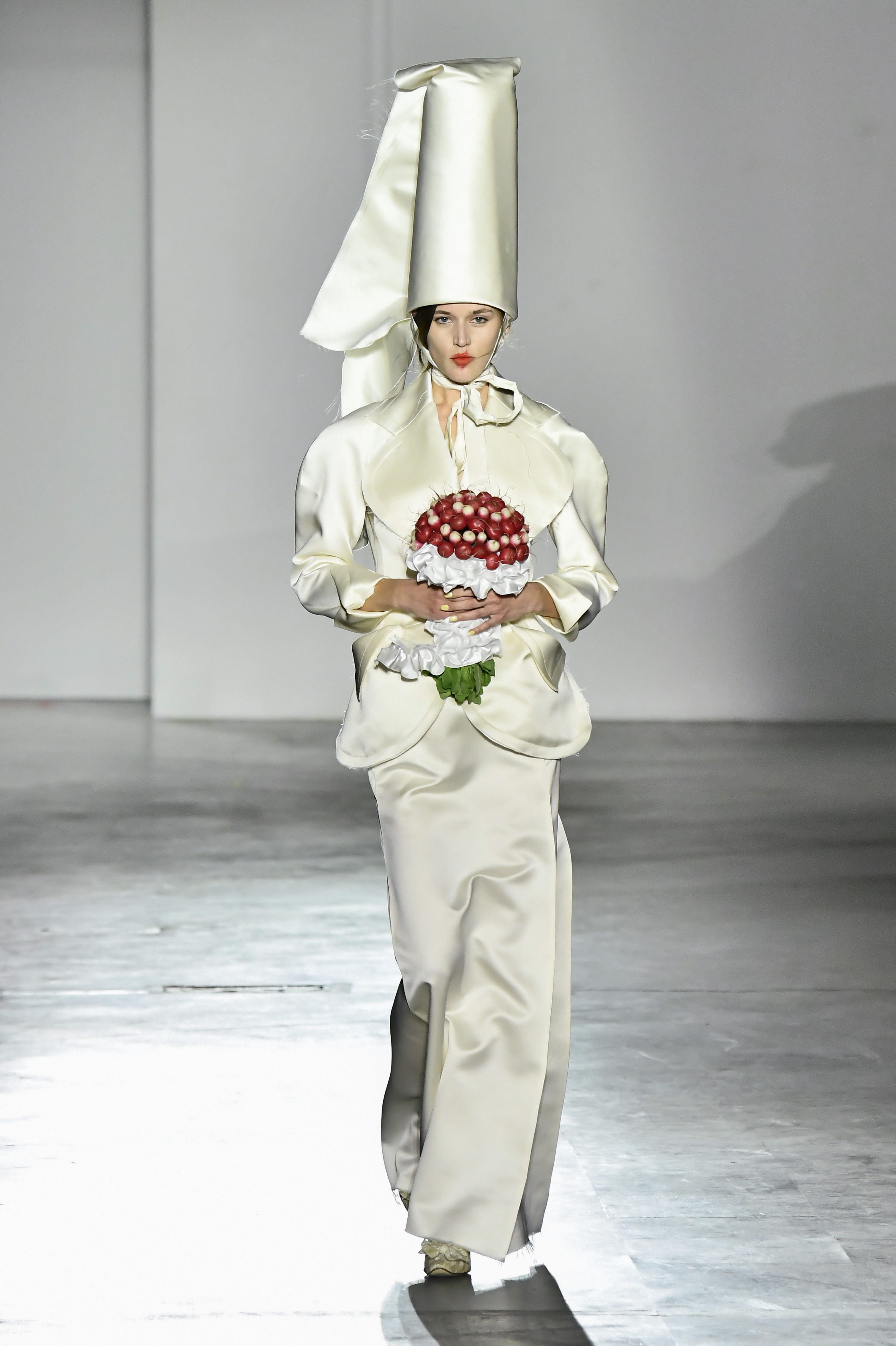 a model wears an ivory skirt suit and carries a radish bouquet.
