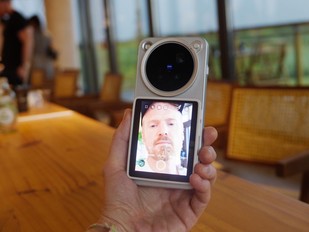 The Vivo X500 Pro Max phone in user's hand, in its dedicated case for magnetic accessories, with Vivo's selfie screen attached, and person is vlogging inside a cafe