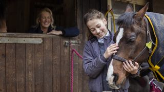 Mother watching on as girl cuddles horse