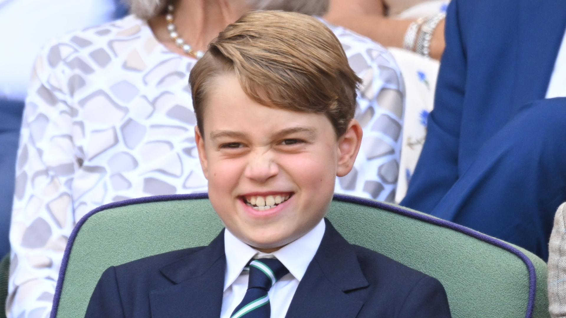 Prince George grins while attending Wimbledon and wearing a navy suit with a white shirt and striped tie