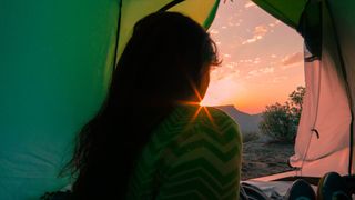 Back of woman's head looking out at sunrise from tent