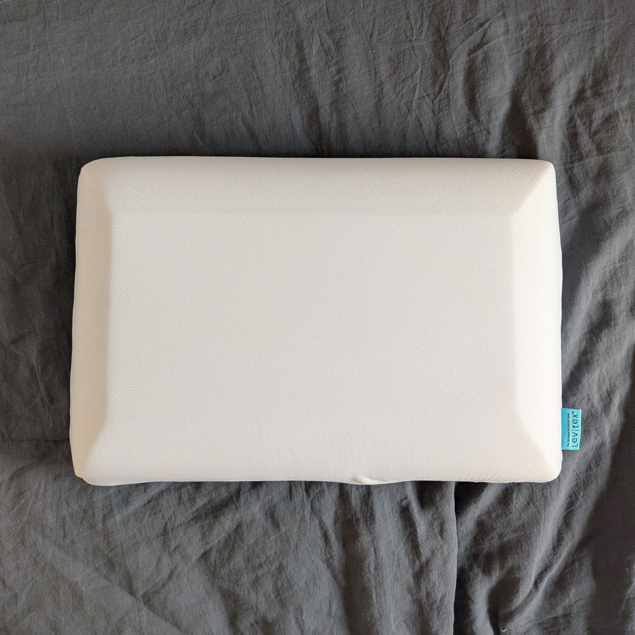 The Levitex Sleep Posture pillow with the foam layer showing through the pillow on a grey bed sheet