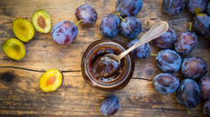 Jar of plum jam next to plums on a wooden surface
