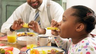 一个小女孩和她的父亲在早餐桌上吃菠萝。