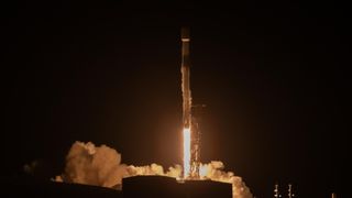 a white rocket lifts off at night above a plume of fire and smoke