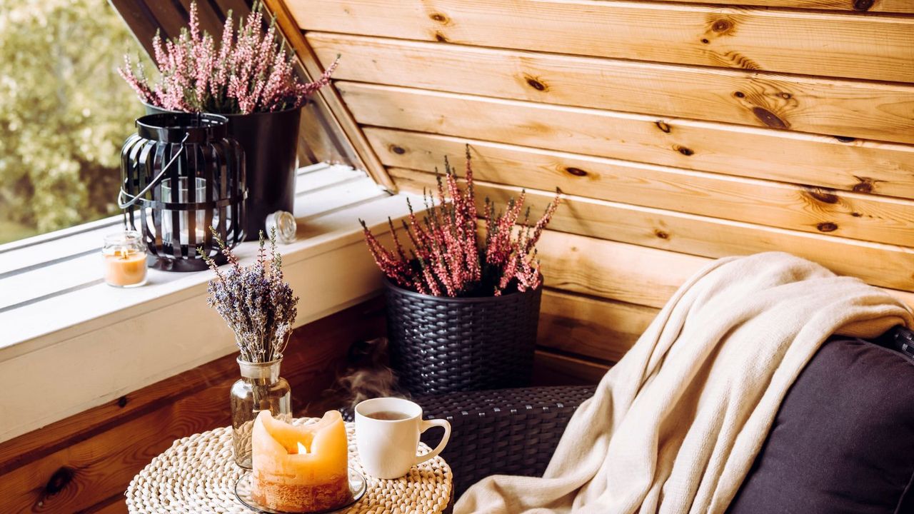 A cozy balcony with a chair covered in a blanket, a light candle, and two pots of lavender plants