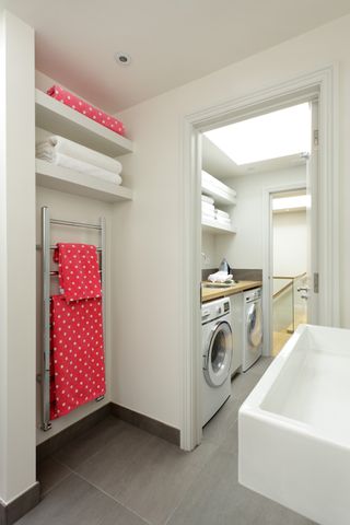 A laundry/utility room with wood worktop, washing machine, tumble dryer and open shelving within a bathroom