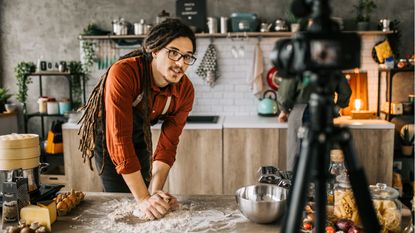 A man kneads bread in a kitchen in front of a camera for his side hustle.