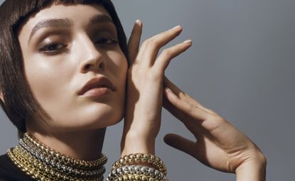 A portrait photo of a female wearing multi-layered necklace and wrist bracelet.