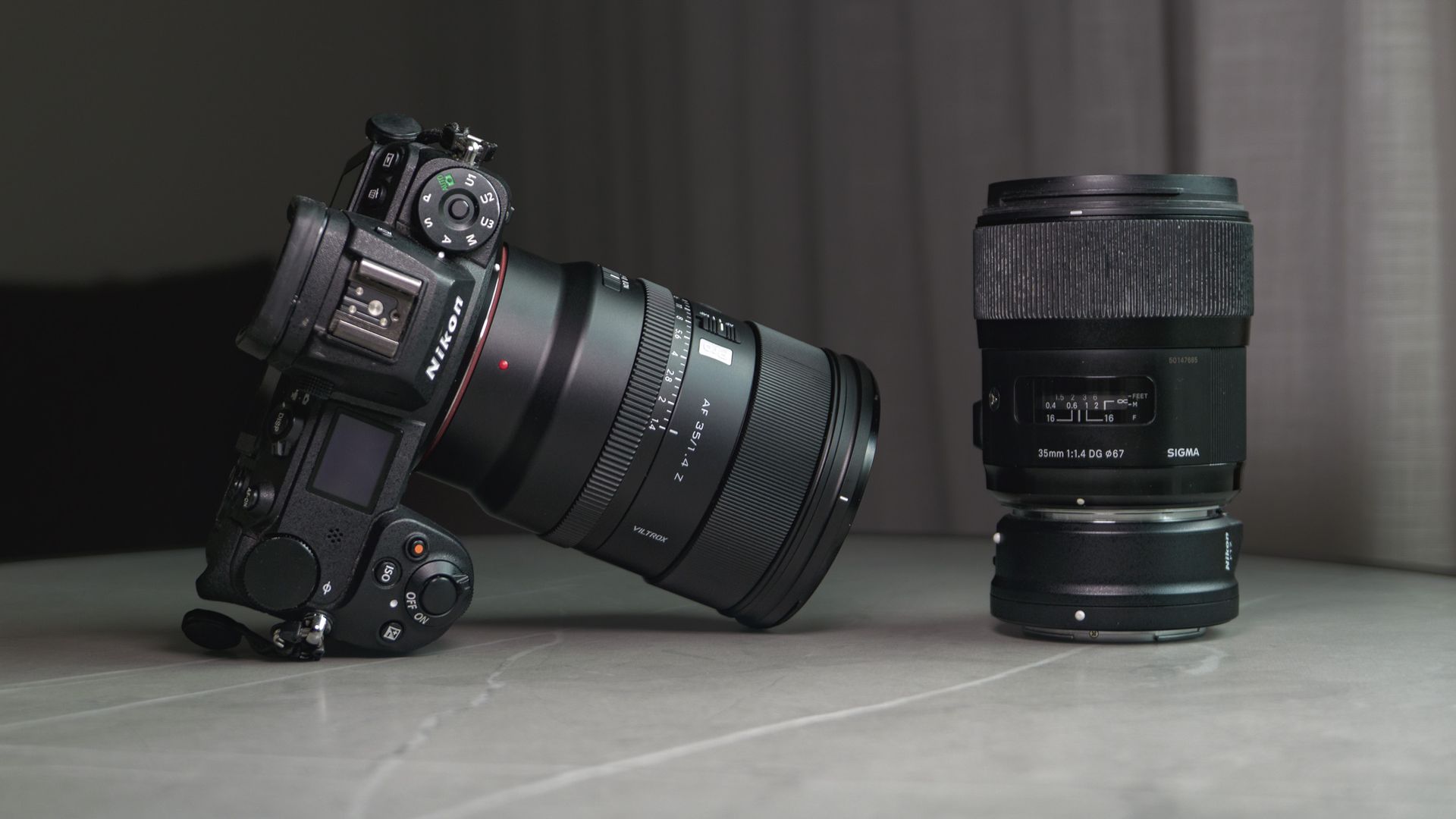 Viltrox AF 35mm F1.4 Pro lens attached to a Nikon mirrorless camera, alongside the Sigma 35mm f1/.4 DG Art lens with Nikon F to Z-mount adapter, on a white marble table