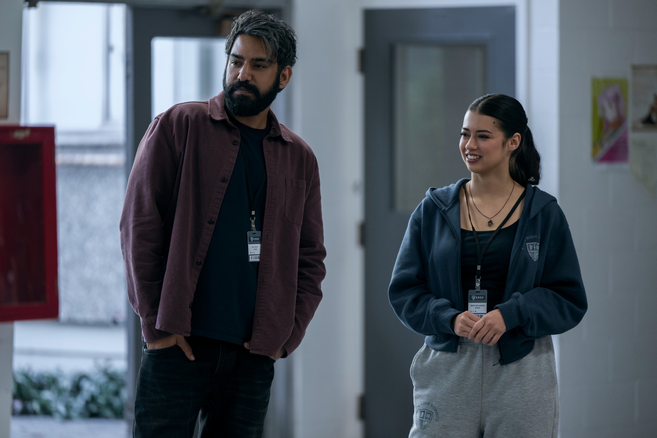 A man with a beard (Rahul Kohli as Seth Peist) and a woman in a gym outfit (Amber Midthunder as Rita Desjardin) stand together in a school building, in Prime Video's 'Carrie.'