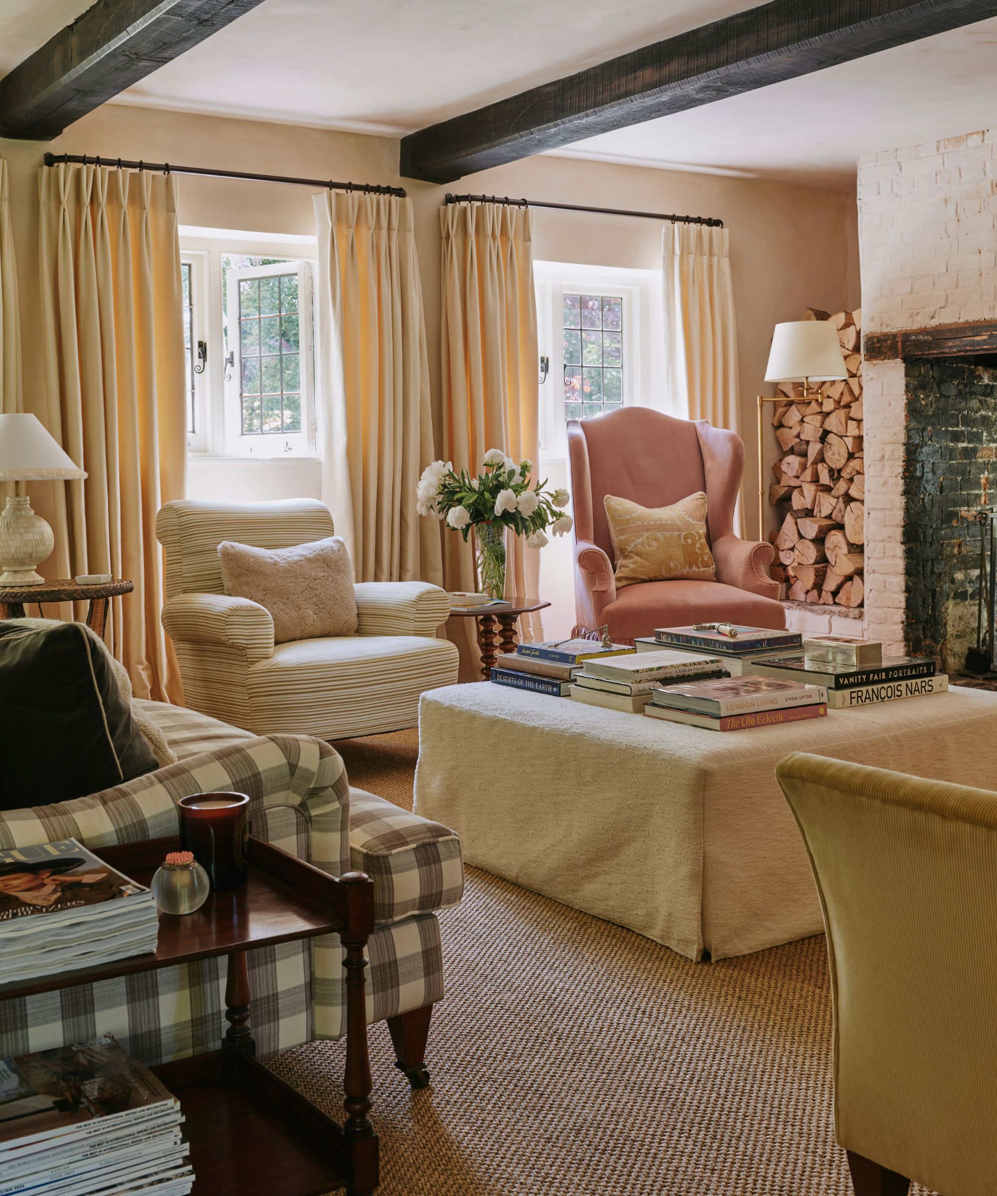country cottage living room with dark wooden beams, a gingham couch, two mismatched armchairs and a neutral living slipcovered ottoman