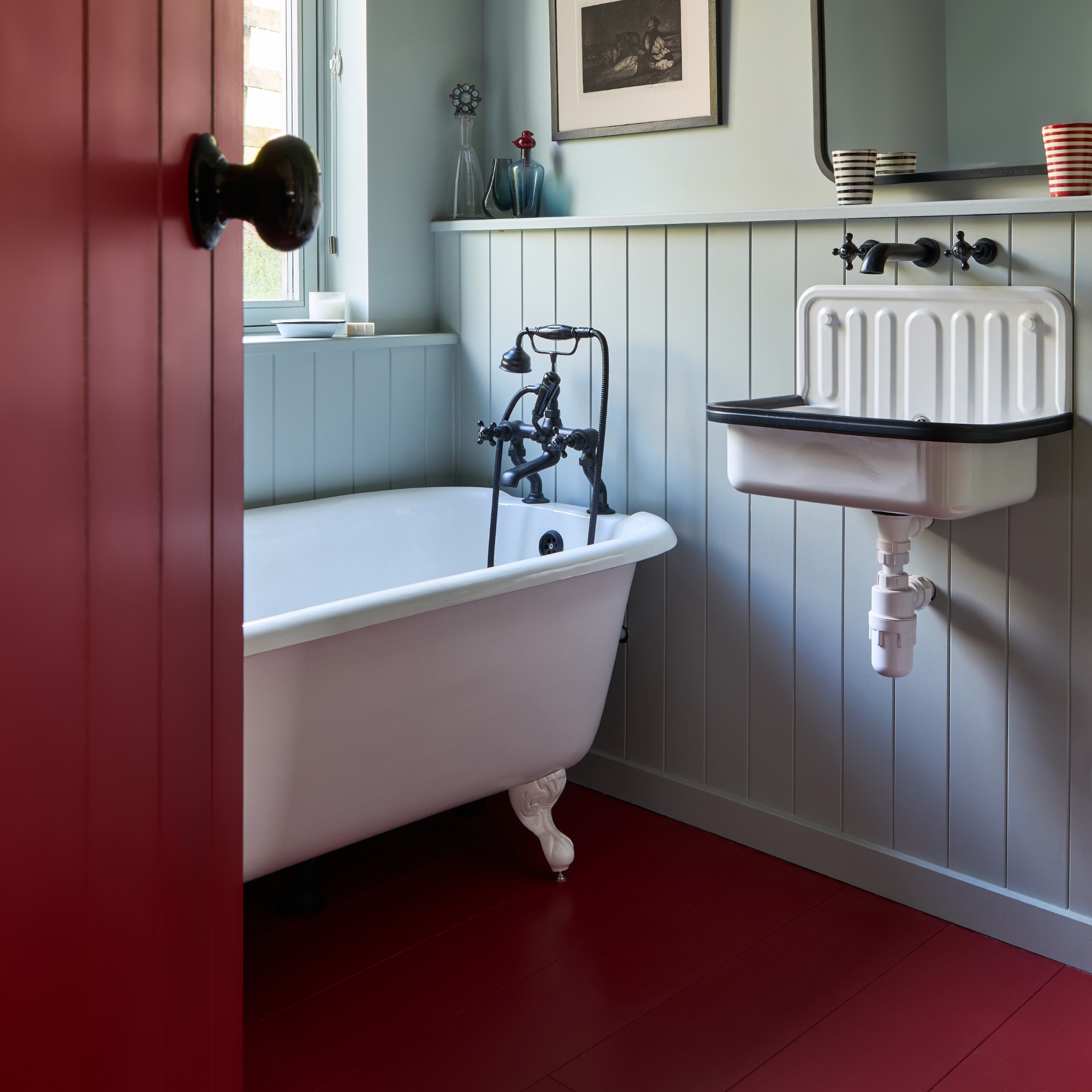 A bathroom painted in a soft blue shade with a contrasting wooden floor painted in dark red matching the door