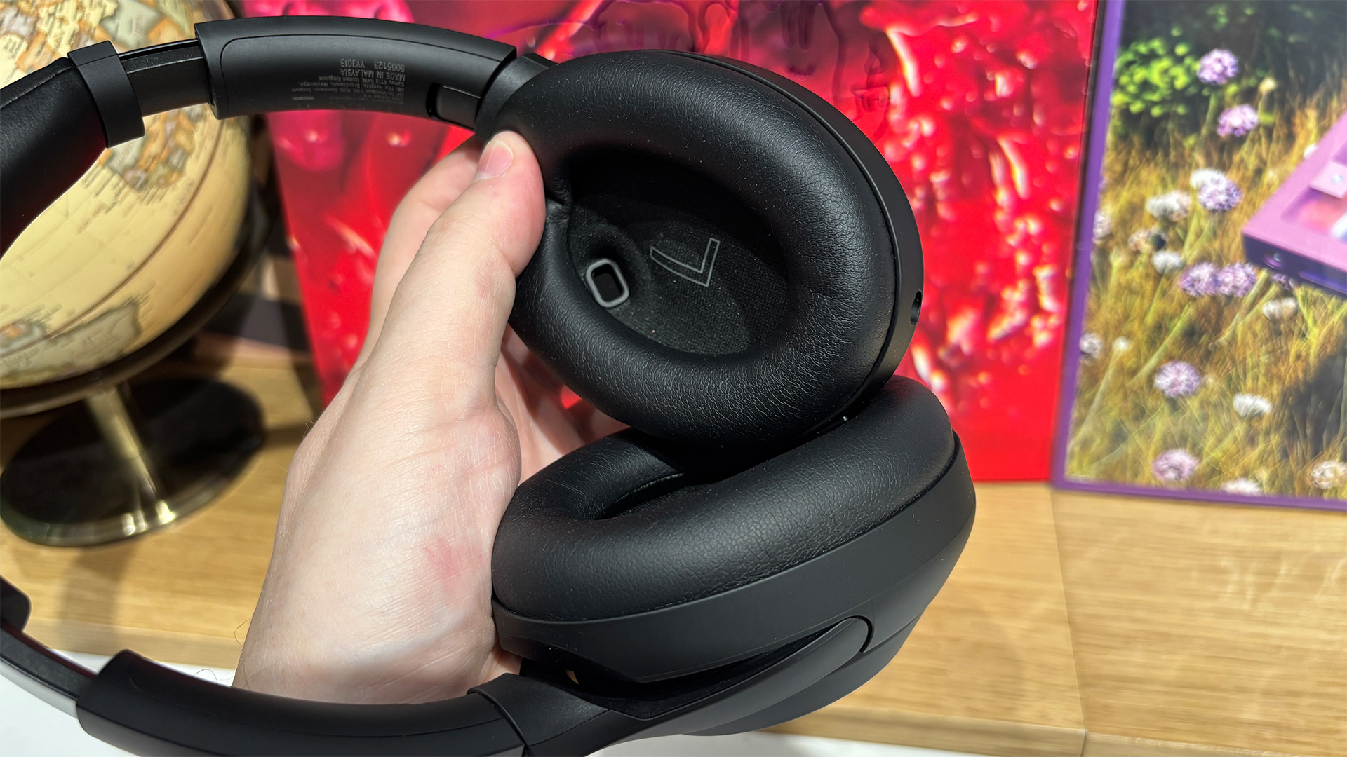 Sony WH-1000XM4C over-ear headphones held in hand in front of busy bookshelf