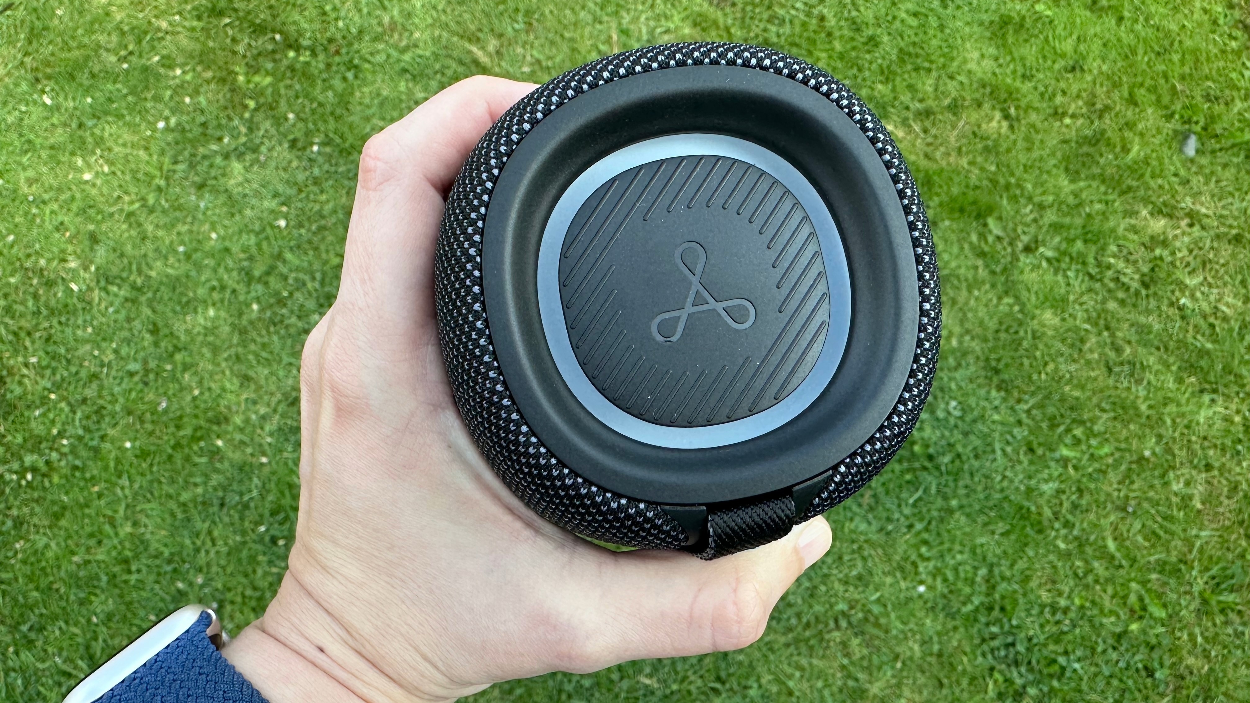 Top panel of the Tribit Stormbox Mini Plus Bluetooth speaker, with RGB lighting, held above a grass surface